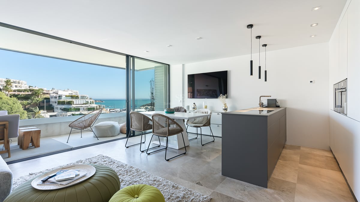 Heller Wohnbereich mit Esstisch, Kücheninsel und Glastüren, die auf eine Terrasse mit Meerblick führen.