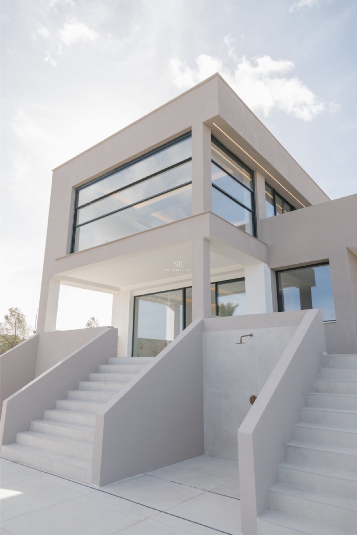 Moderne Villa mit großen Glasfronten und minimalistischen weißen Betontreppen unter hellem Himmel.