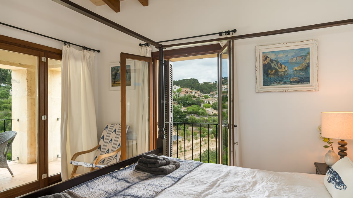 Chambre de style méditerranéen avec un lit à baldaquin en bois sombre et balcon offrant une vue sur les collines.