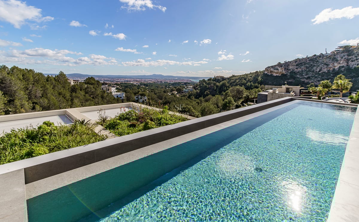Une piscine à débordement à l'eau bleue claire surplombant une vallée verdoyante et une ville lointaine.