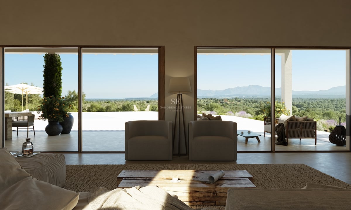 Salon minimaliste avec de grandes baies vitrées ouvrant sur une terrasse surplombant la vallée et les montagnes.