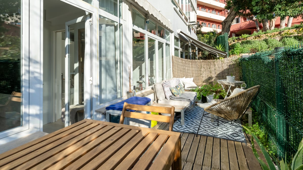 Private wooden terrace with outdoor lounge furniture, geometric rug, and glass sliding doors under bright daylight.