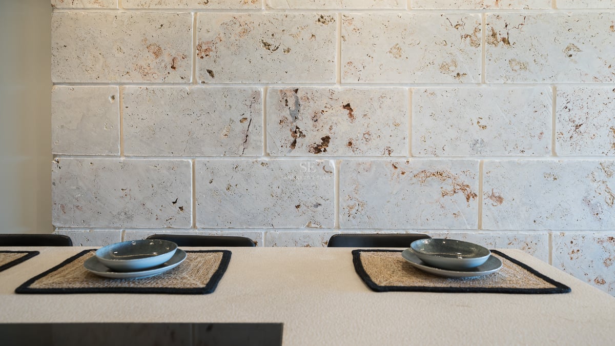 Gros plan d'un mur en blocs de travertin derrière une table avec des sets de table en fibres et bols en céramique.