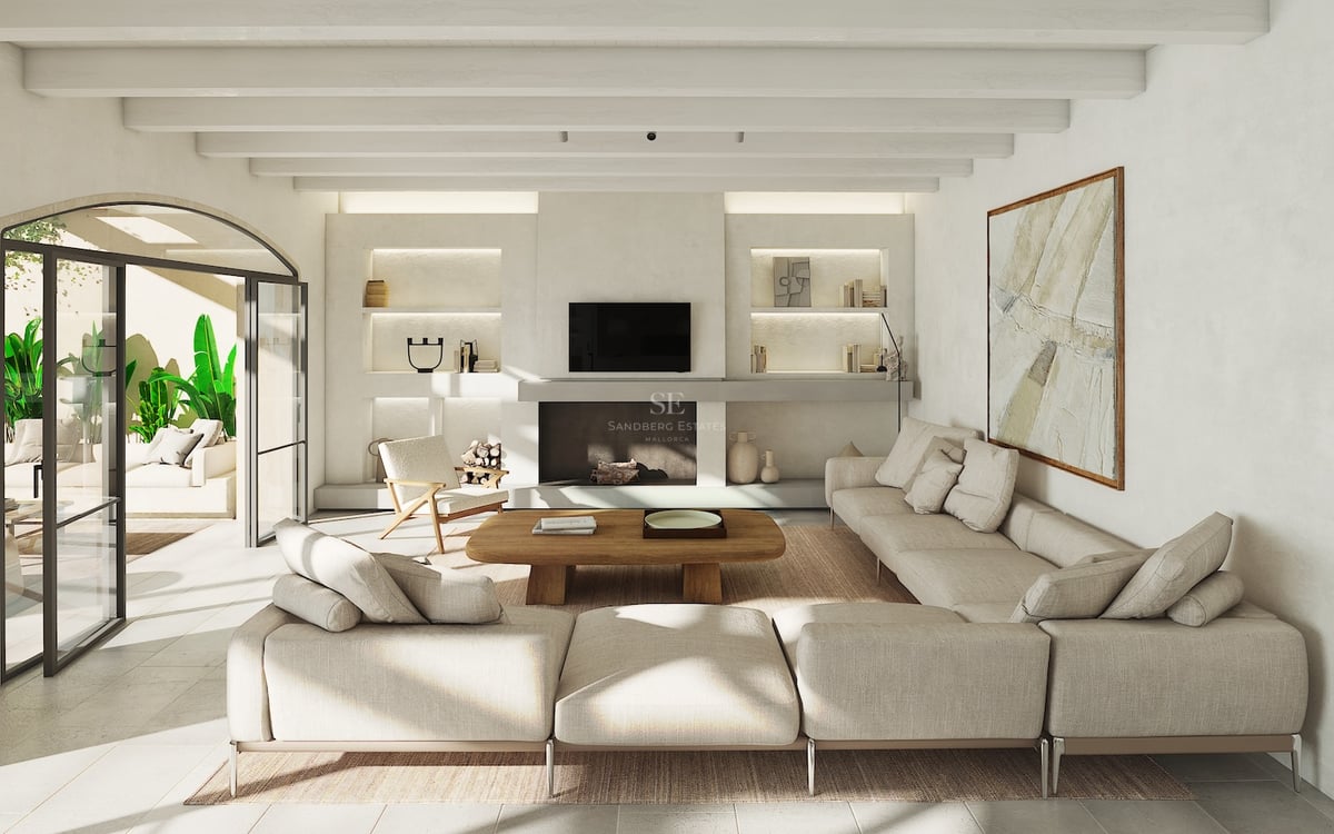 Salon baigné de lumière avec canapé beige, poutres apparentes et accès à une terrasse via une porte voûtée.