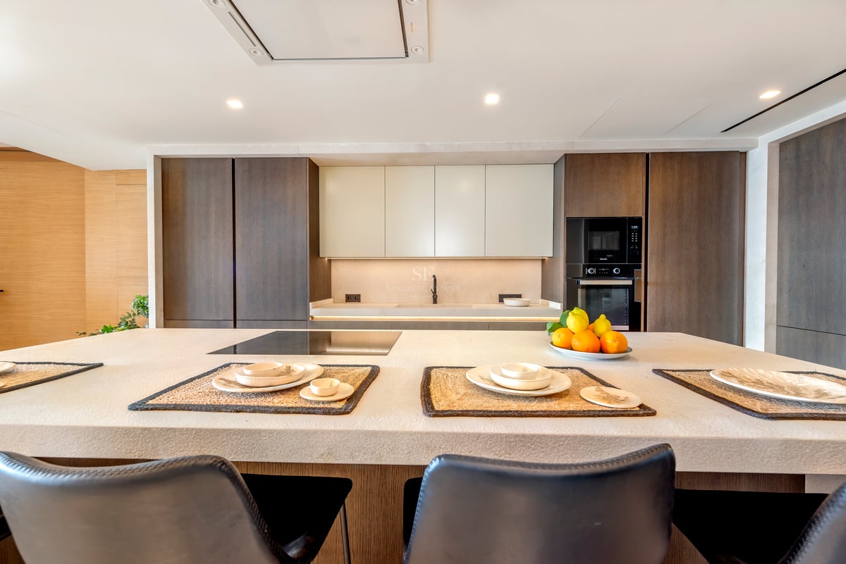 Cuisine moderne avec un grand îlot en pierre, des armoires en bois sombre et des appareils électroménagers intégrés.