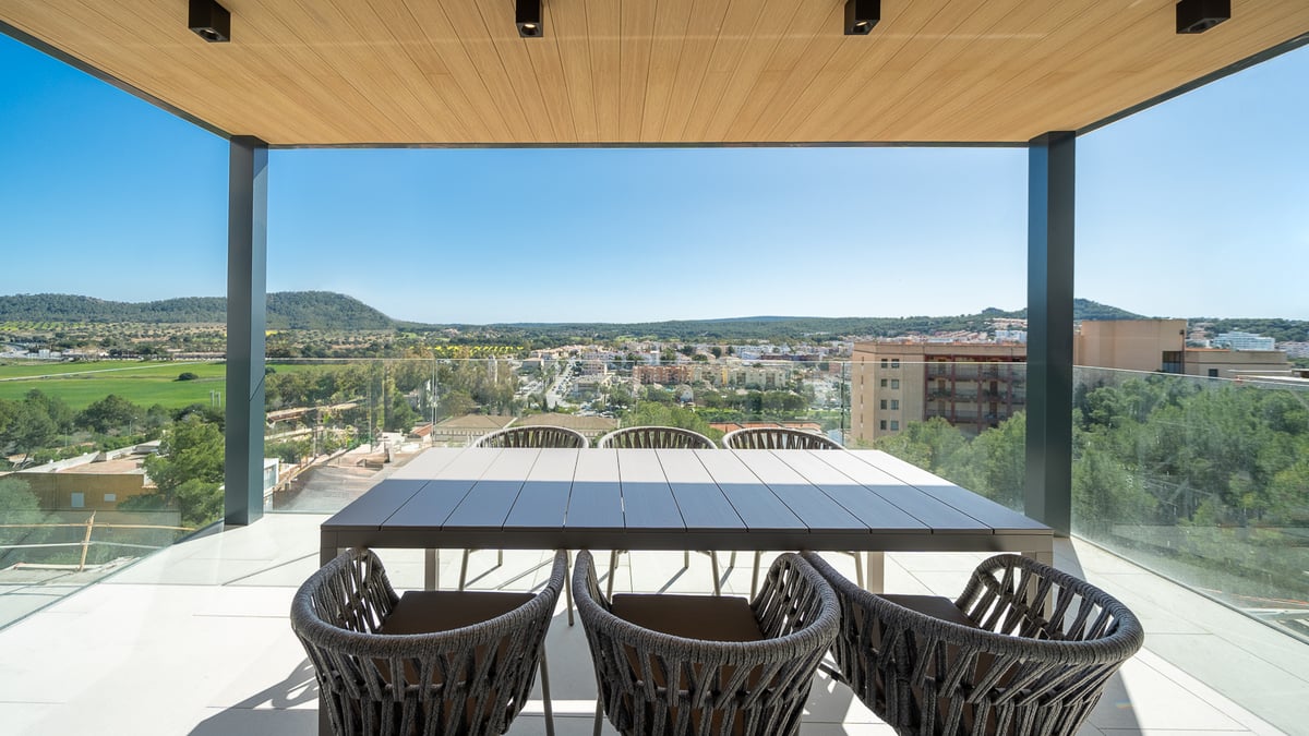 Terrasse moderne avec plafond en bois, table à manger et garde-corps en verre donnant sur une vallée verdoyante.