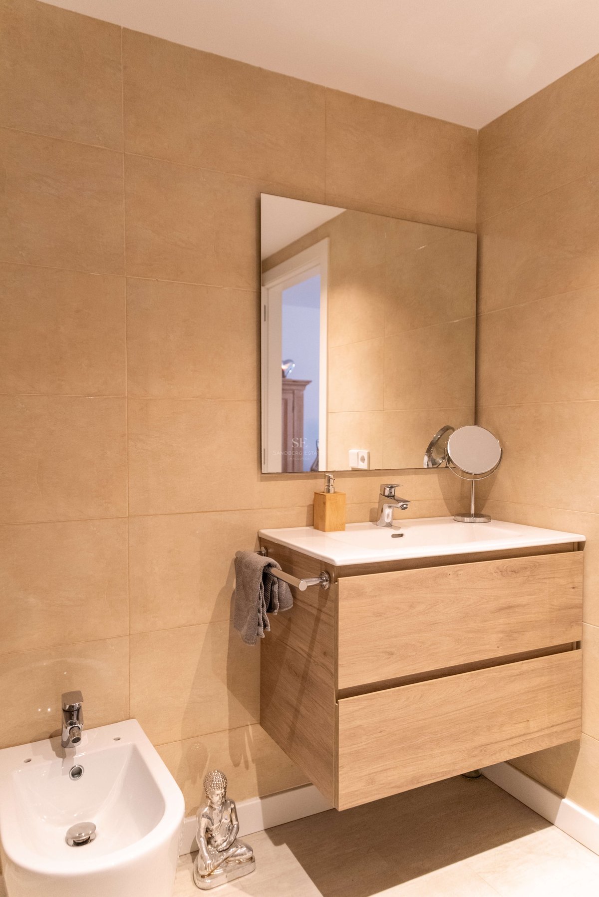 Modernes Bad mit schwebendem Eichen-Waschtisch, weißem Keramikbecken, großem Spiegel und sandfarbenen Fliesen.