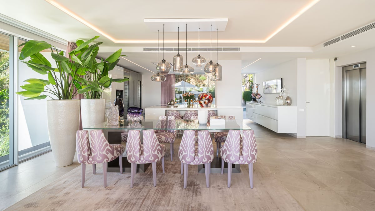 Moderner Essraum mit Glastisch, gemusterten lavendelfarbenen Stühlen und Designer-Glaspendelleuchten.