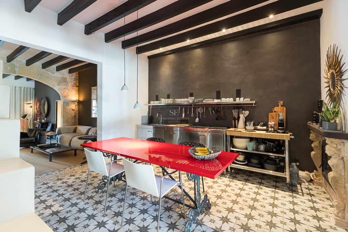 Cuisine industrielle moderne avec table rouge vif, sol en carreaux de ciment et poutres en bois sombre apparentes.