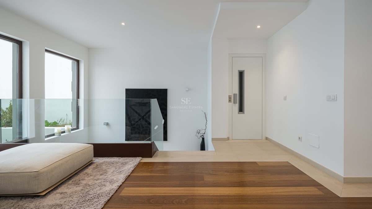 Palier moderne avec garde-corps en verre, parquet en chêne et porte d'ascenseur blanche.