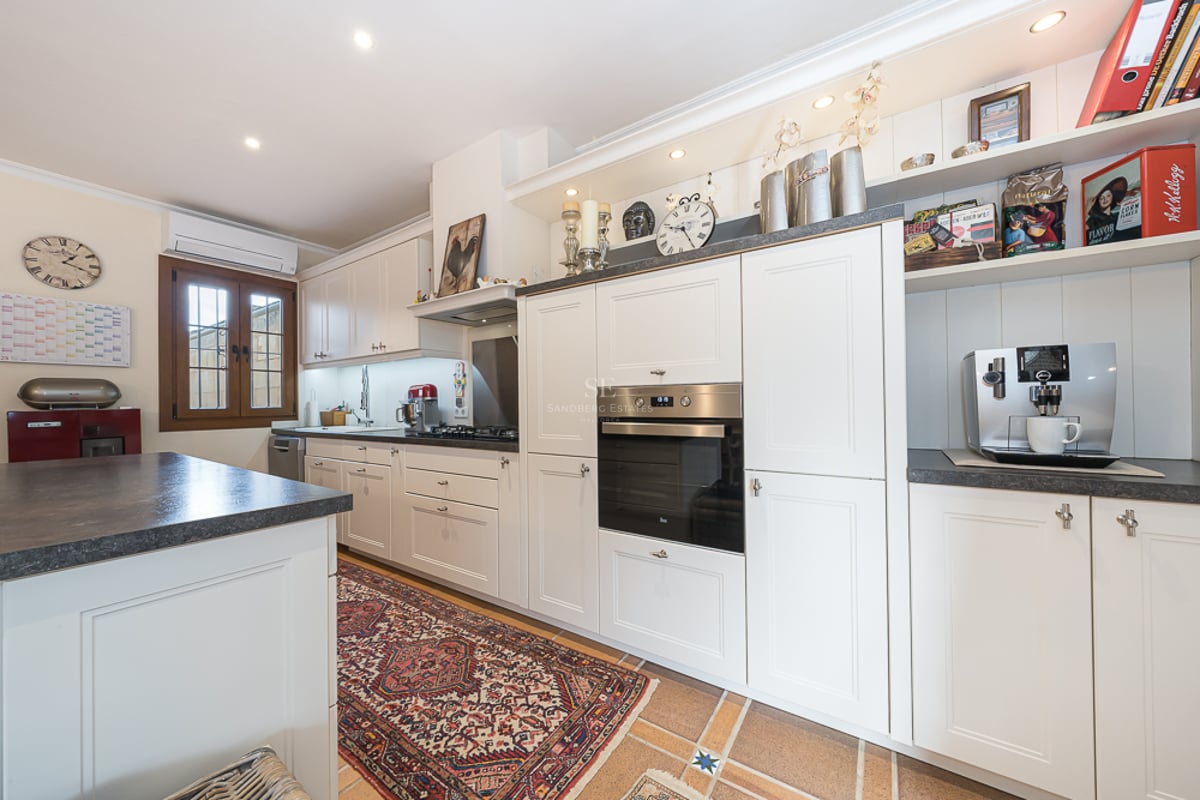 Cuisine blanche avec plans de travail sombres, four encastré et tapis de style oriental sur sol carrelé.