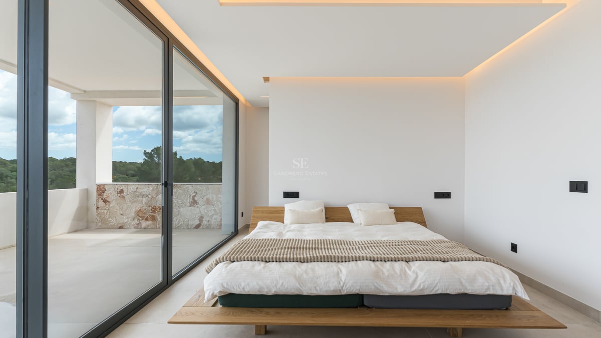 Minimalistisches Schlafzimmer mit Holzbett, großen Glasschiebetüren und Zugang zum Balkon mit Natursteinmauer.