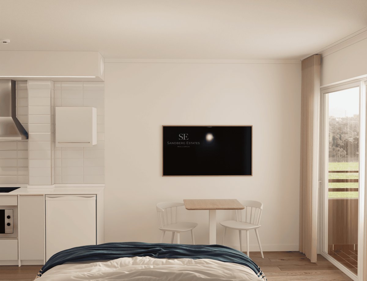 Vue d'un studio montrant un lit, une petite table à manger sous une télé, une cuisine blanche compacte et un balcon.