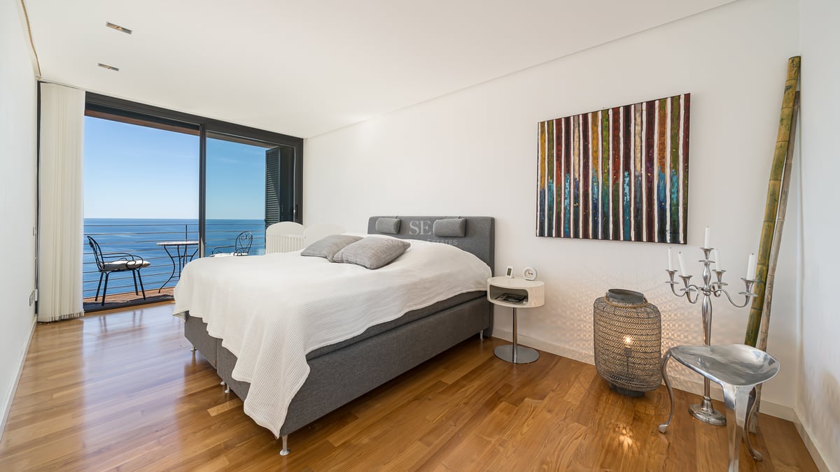 Modern bedroom featuring oak floors and floor-to-ceiling glass doors opening to a Mediterranean sea view.