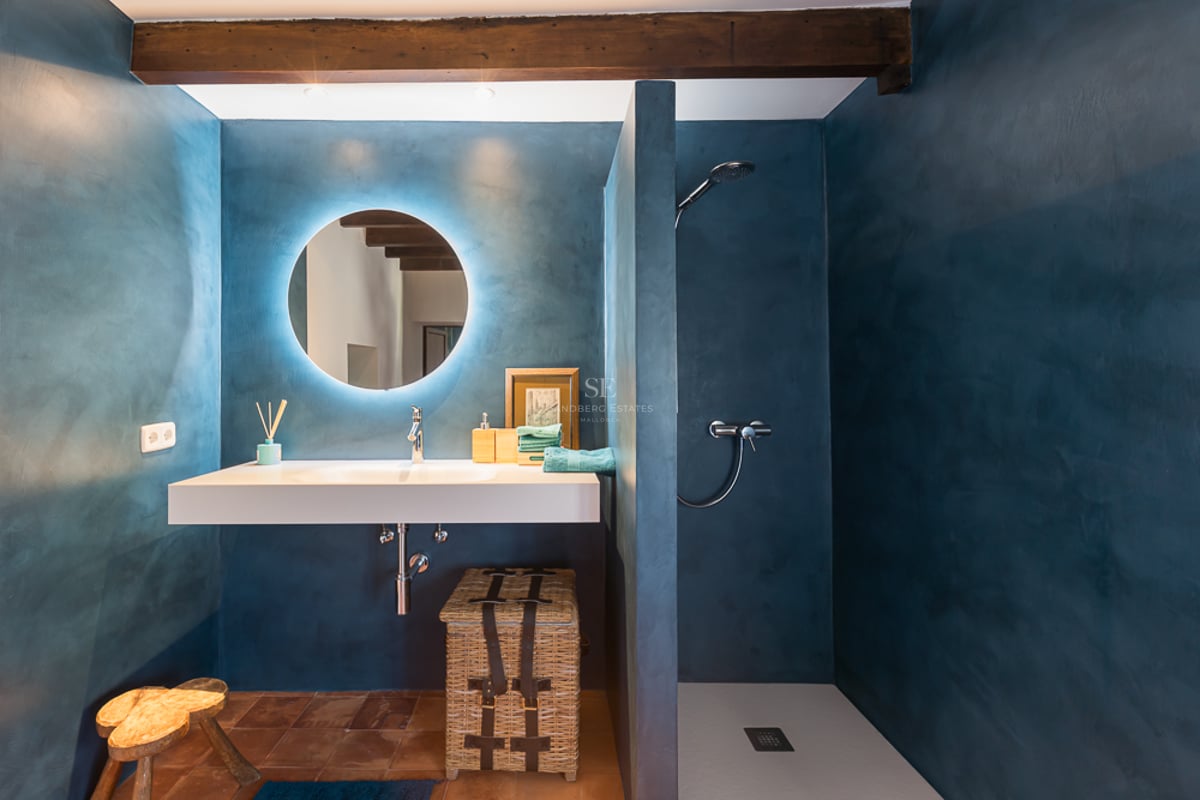 Salle de bain moderne avec murs en microciment bleu, miroir circulaire rétroéclairé et sol en terre cuite.