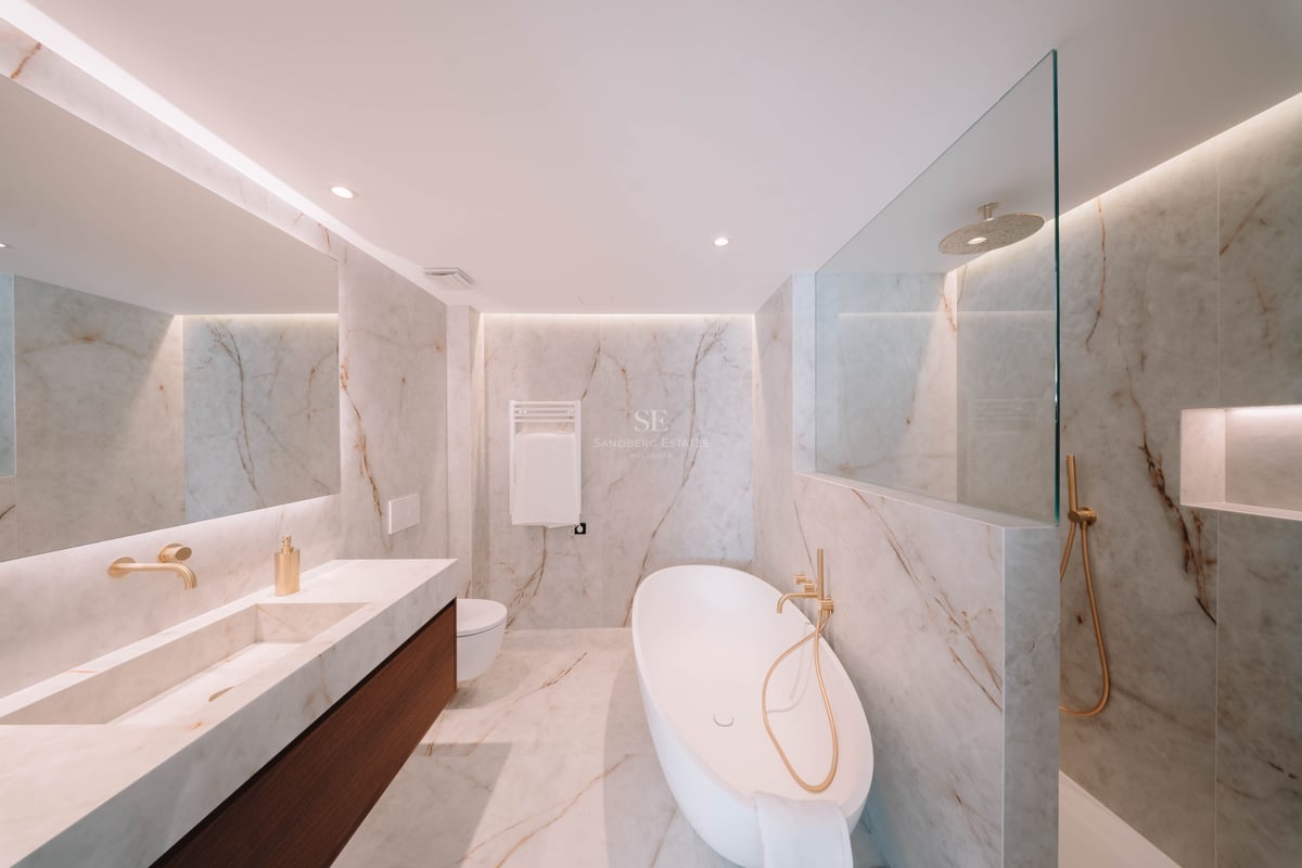 Salle de bain moderne en marbre avec baignoire îlot blanche, robinetterie dorée et double vasque.