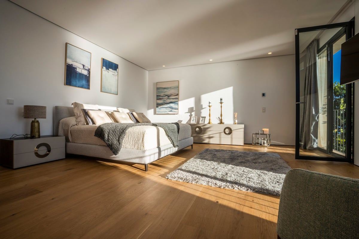 Modernes Schlafzimmer mit großem Bett, hellem Eichenboden, Balkontür und intensivem natürlichem Lichteinfall.