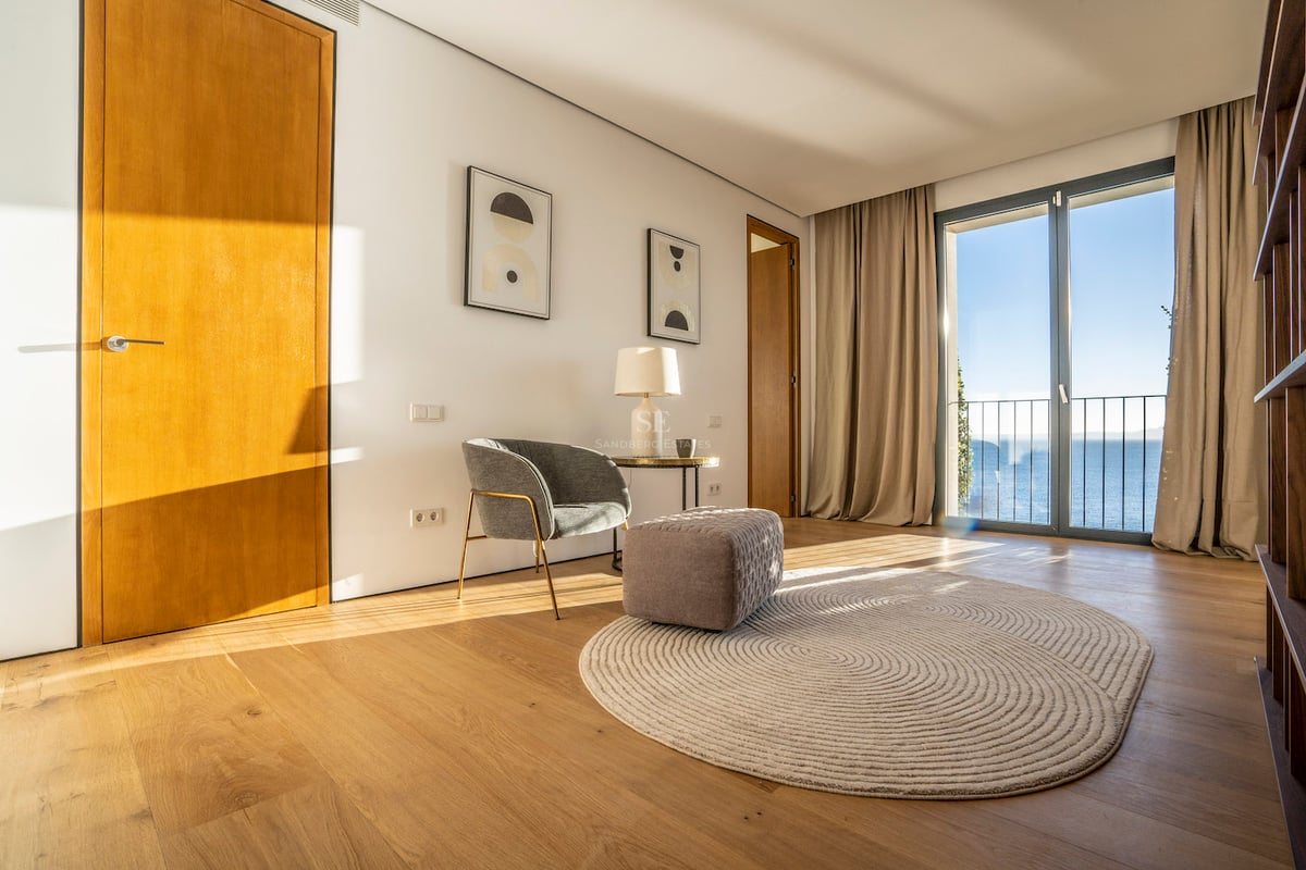 Modernes Zimmer mit Eichenparkett, grauem Sessel und Glastüren mit Blick auf das Mittelmeer.