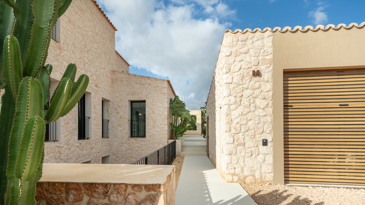 Minimalistisk naturstensgång mellan två samtida villabyggnader under en klarblå himmel.