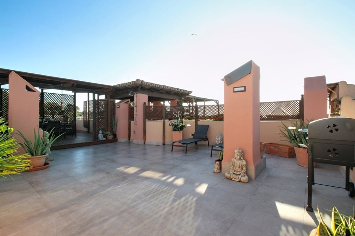 Medelhavstak-terrass med terrakotta-väggar, träpergola, stengolv och solstolar under en klarblå himmel.