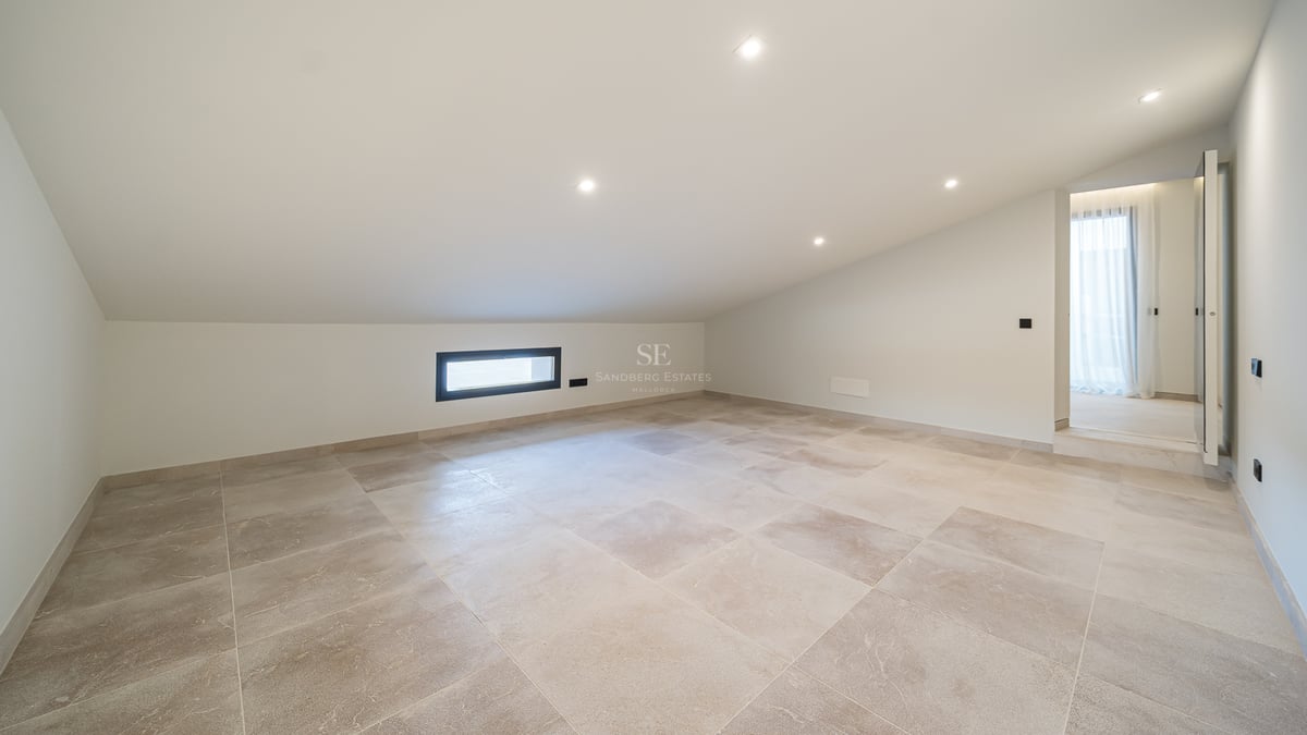 Pièce vide avec plafond incliné blanc, carrelage en pierre beige et spots encastrés.