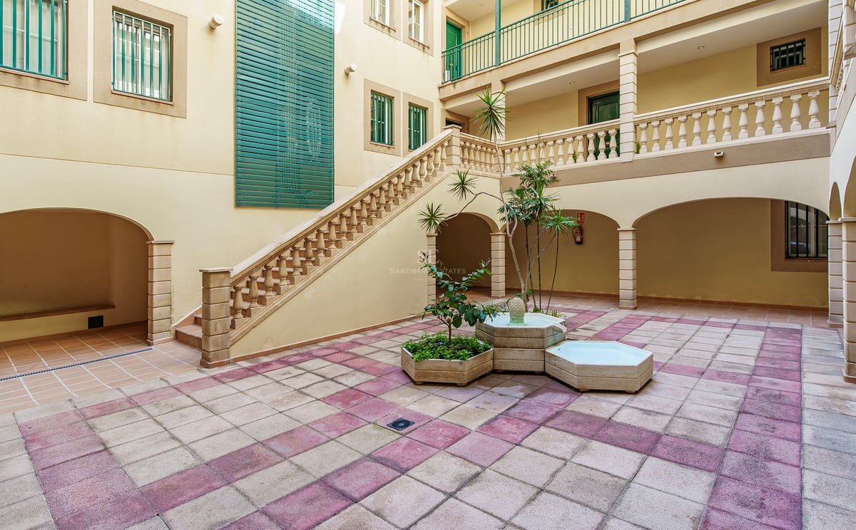 Innergård med schackrutigt golv, stenfontän, storslagen trappa med balustrad och klassiska valv.