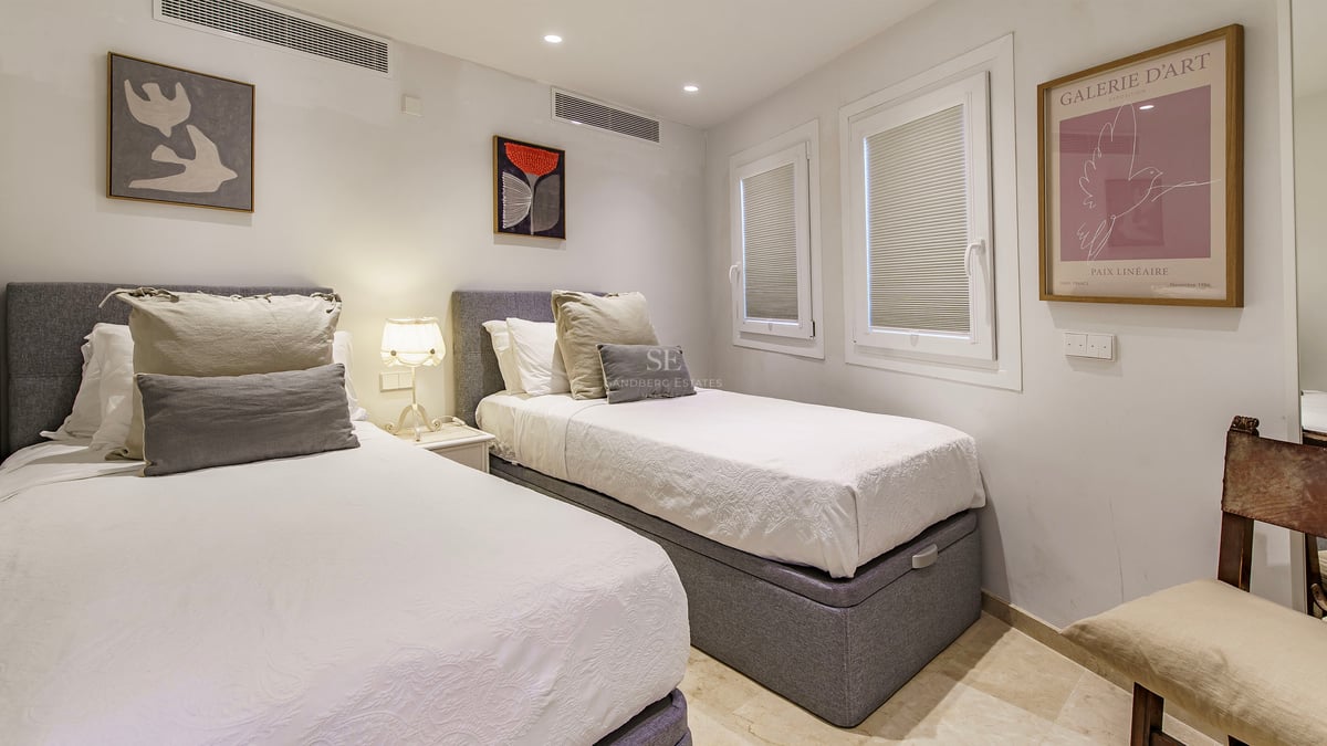 Bedroom with two single beds, grey headboards, white linens, and contemporary wall art.