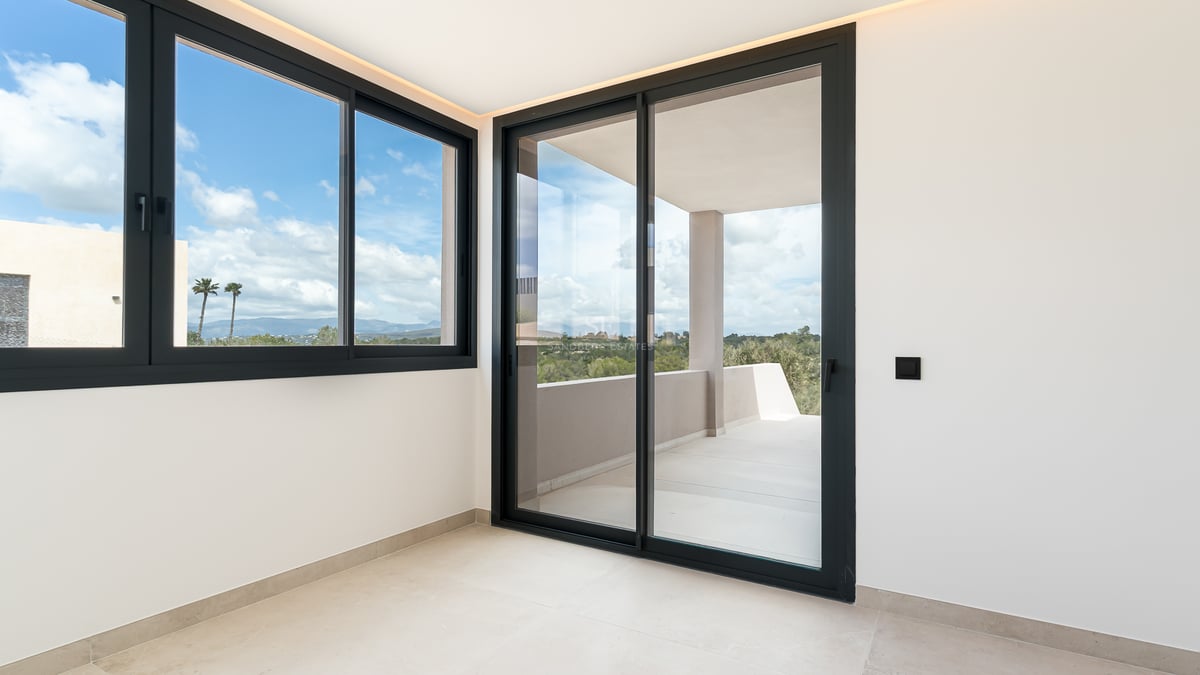 Heller moderner Raum mit großen Schiebefenstern mit schwarzem Rahmen, die auf eine sonnige private Terrasse führen.