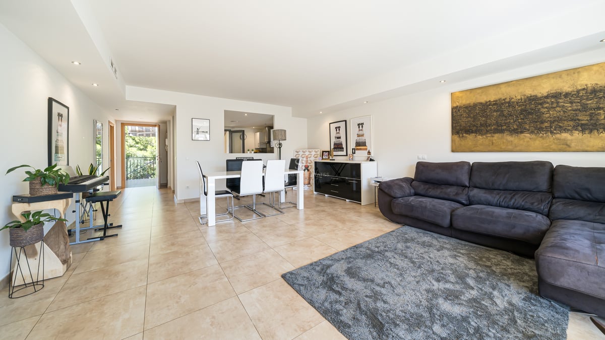 Rymligt vardagsrum med grå soffa, vit matgrupp, klinkergolv och utgång till solig terrass.