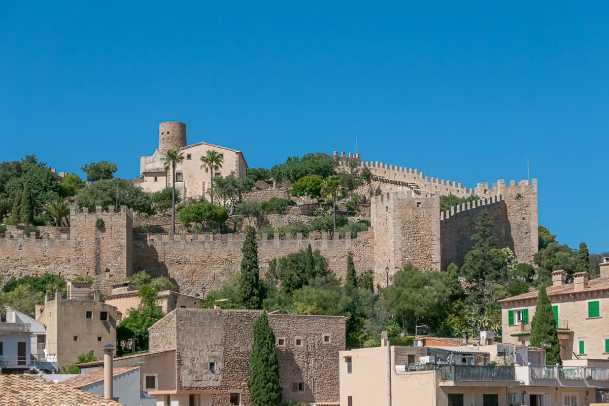 Murs et tours en pierre d'une forteresse médiévale sur une colline sous un ciel bleu dans un village majorquin.