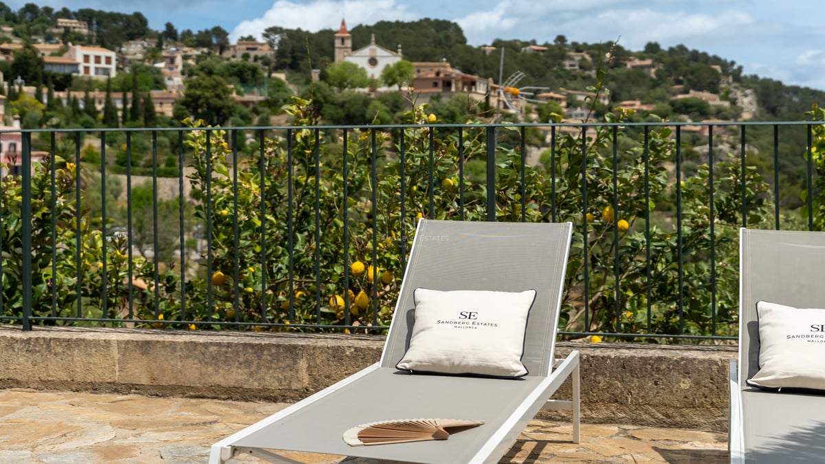 Chaise longue moderne sur une terrasse en pierre surplombant un citronnier et un village méditerranéen perché.
