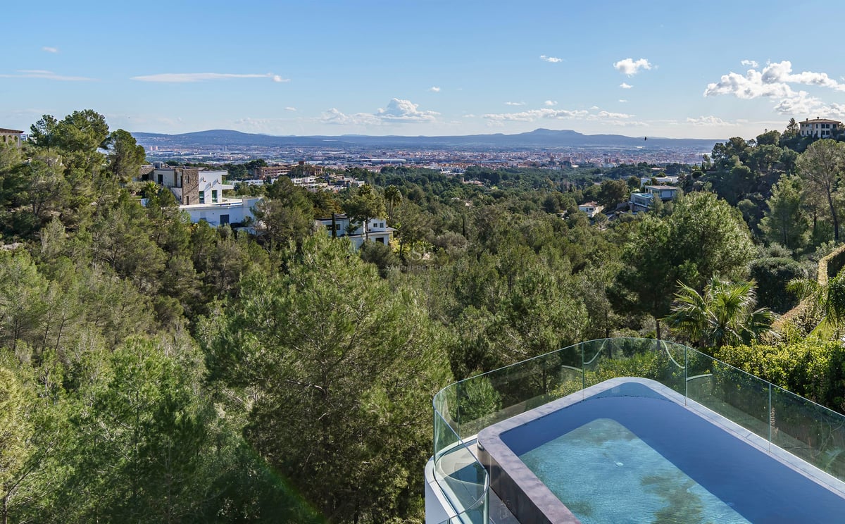 Une piscine à débordement avec garde-corps en verre surplombant une vallée verdoyante, la ville et les montagnes.