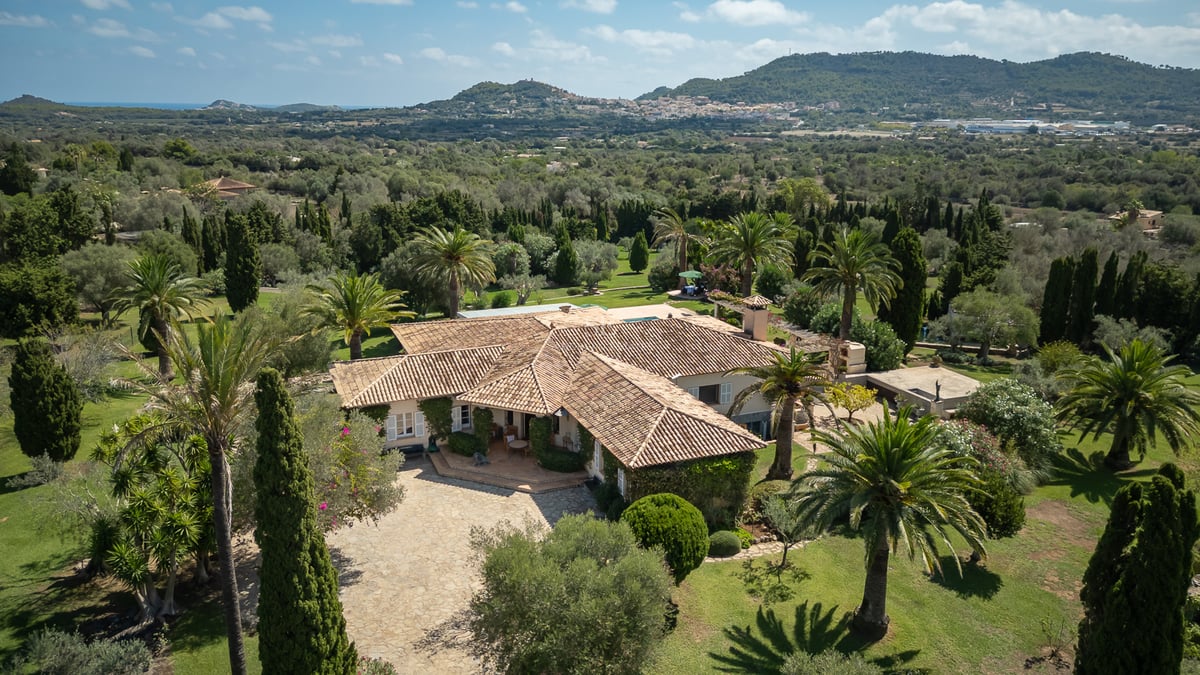 Vue aérienne d'une villa méditerranéenne aux toits de tuiles, entourée de palmiers et d'un vaste jardin paysager.