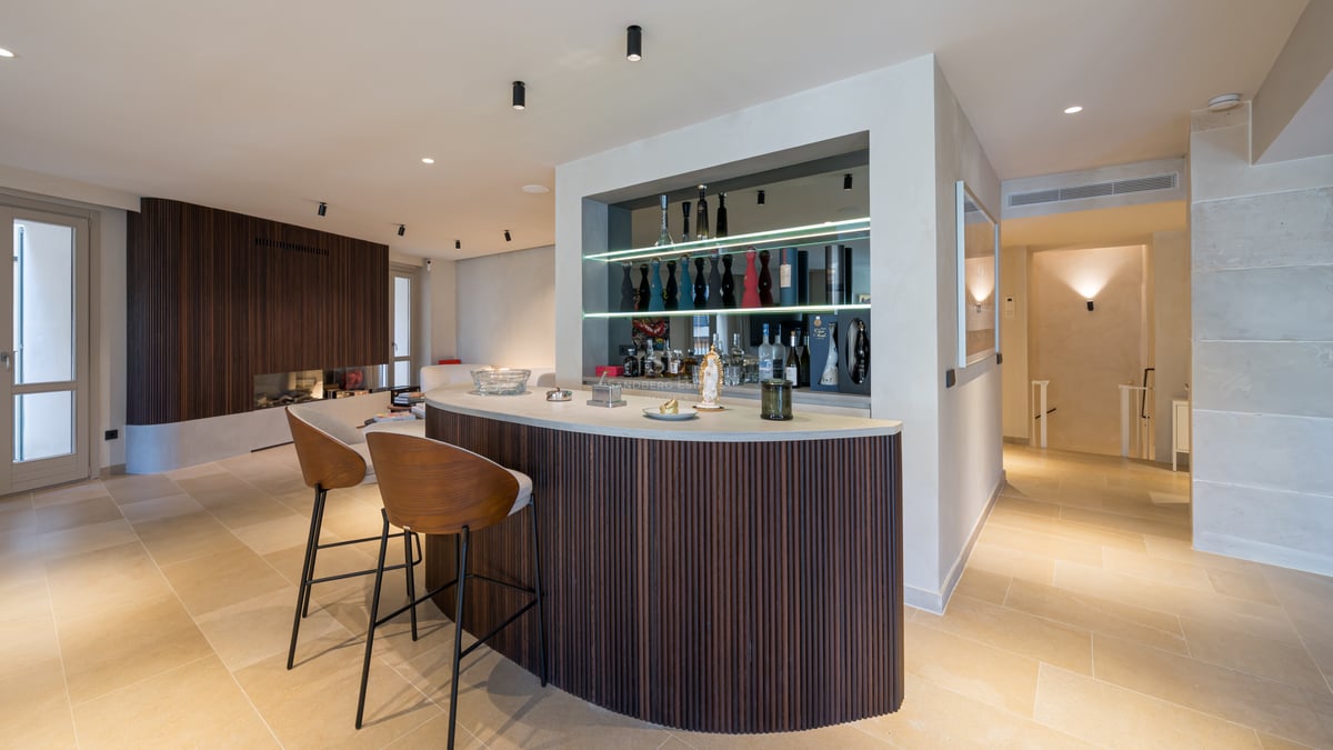 Bar incurvé en bois avec comptoir en pierre, étagères en verre éclairées et tabourets modernes.