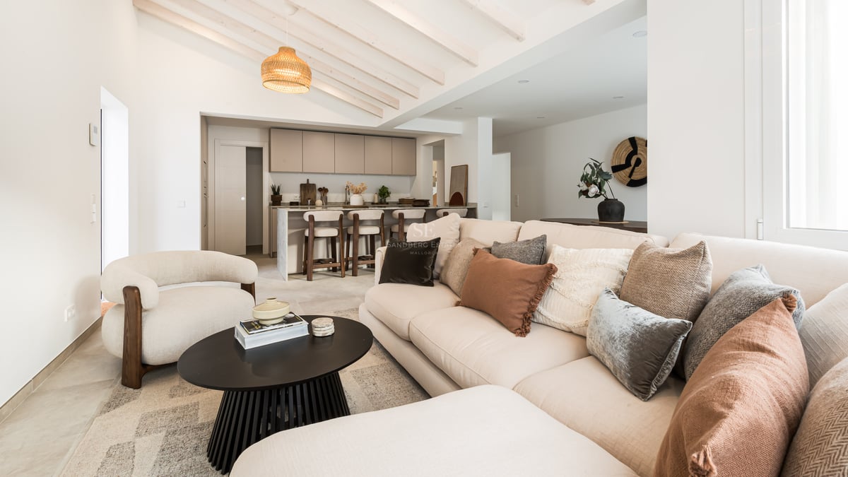 Bright living room with beige sofa, wooden ceiling beams, and a modern kitchen island in the background.
