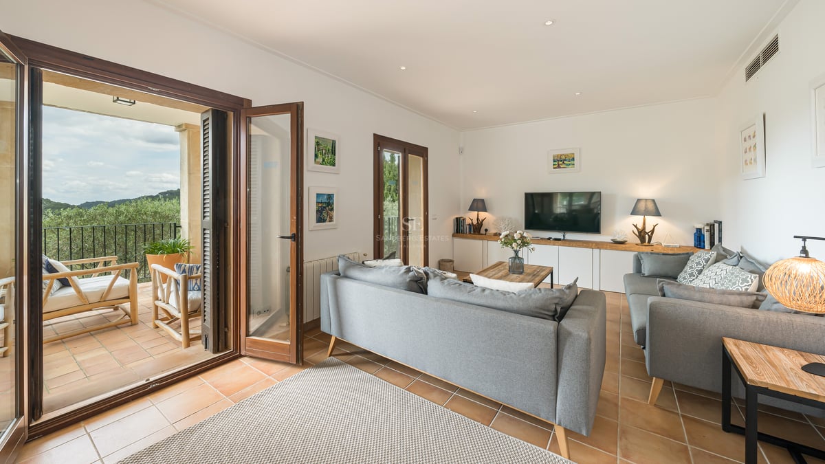 Canapé gris moderne dans un salon avec sol en terre cuite et portes-fenêtres ouvrant sur une terrasse.