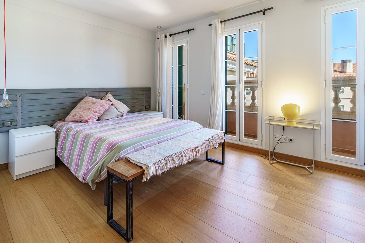 Ljust sovrum med ekparkett, dubbelsäng och altandörrar som leder ut till en klassisk balkong.