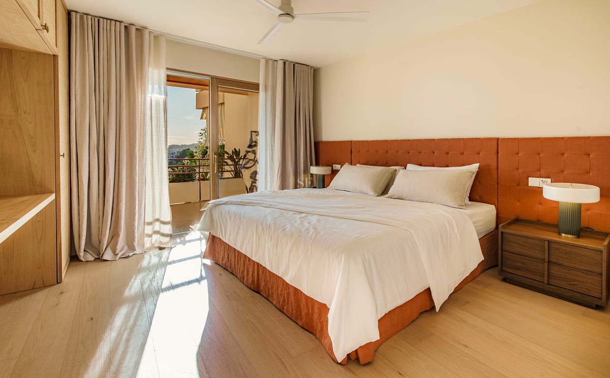 Geräumiges modernes Schlafzimmer mit orangefarbenem Kopfteil, Holzboden und Glasschiebetür zu einer sonnigen Terrasse.