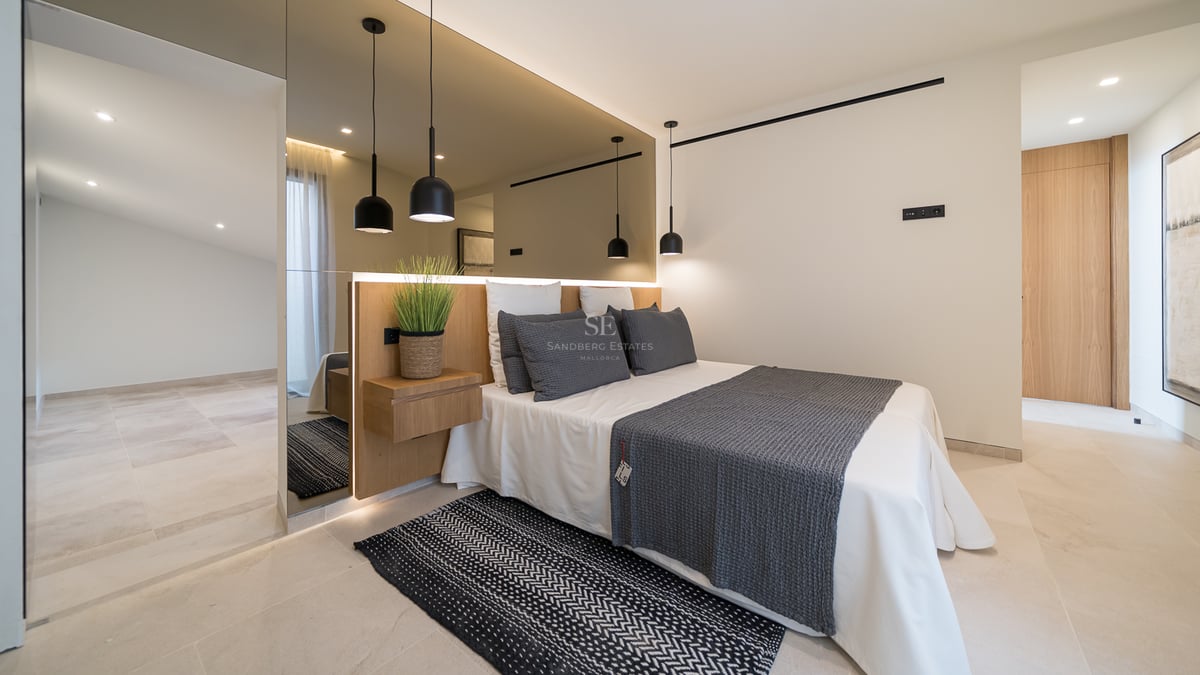 Chambre moderne avec un grand mur de miroirs derrière le lit, suspensions noires et sol en pierre claire.