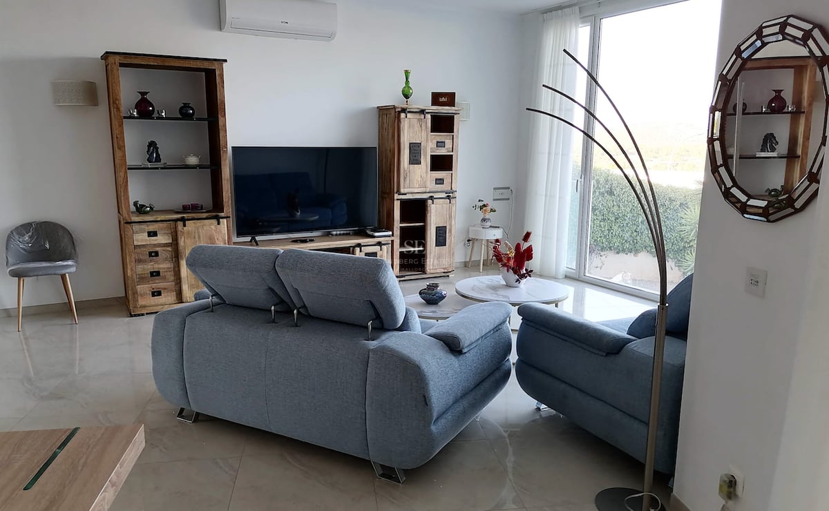 Salon moderne avec canapés bleus, meubles en bois massif, sol en grès cérame poli et grande baie vitrée.