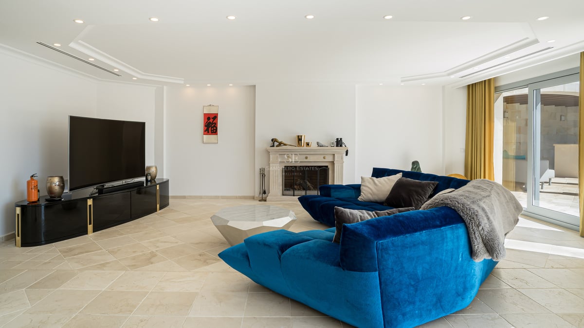 Moderner Wohnbereich mit blauem Samtsofa, Steinkamin und Natursteinboden unter LED-Einbaustrahlern.