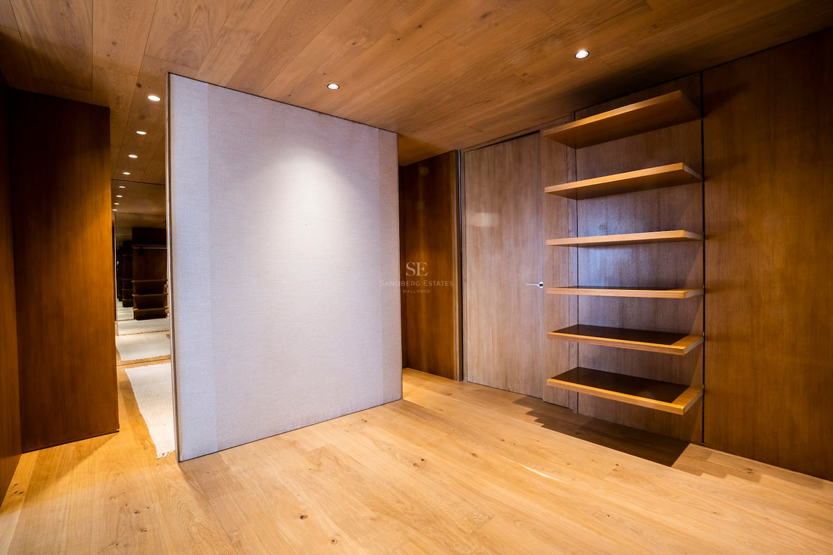 Minimalistisches Ankleidezimmer mit Wänden und Decke aus Eichenholz, Einbauregalen und warmer Beleuchtung.