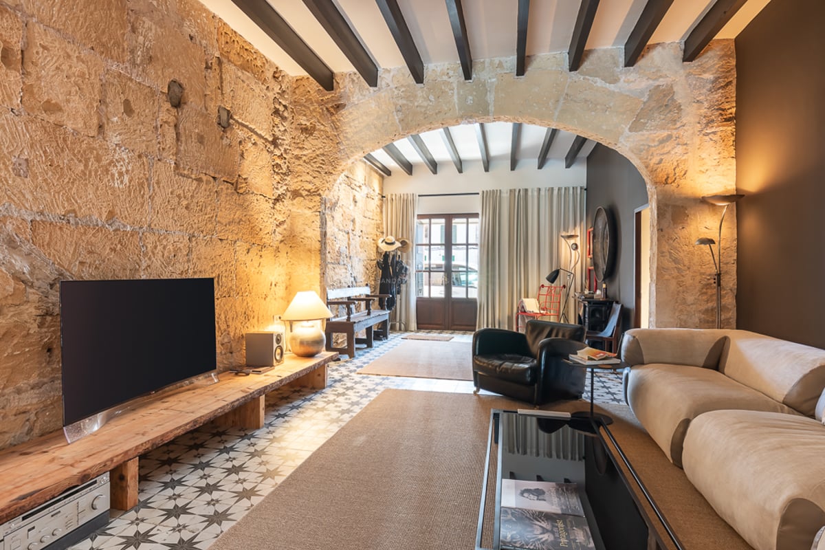 Salon moderne avec murs en pierre d'origine, arche, poutres apparentes et carrelage hydraulique traditionnel.