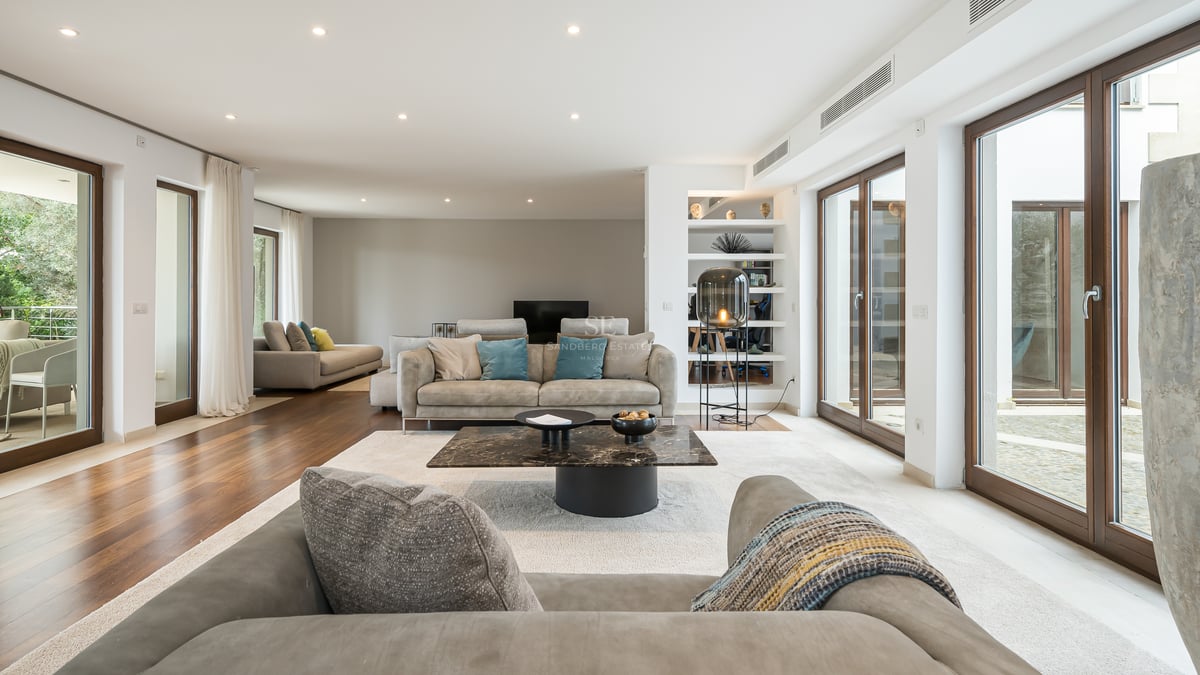 Grand salon moderne avec parquet, canapés gris contemporains, table basse en marbre et grandes baies vitrées.