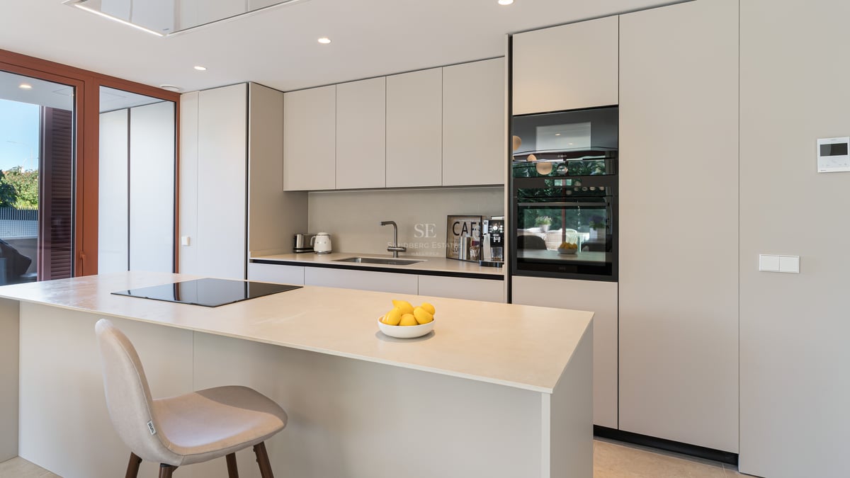 Modern sand-toned kitchen featuring a central island, integrated induction hob, and built-in designer appliances.
