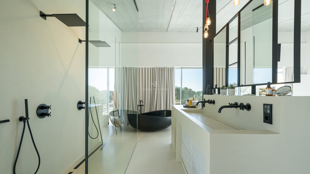 Minimalistiskt badrum med svart fristående badkar, dubbelhandfat och stora fönsterpartier.