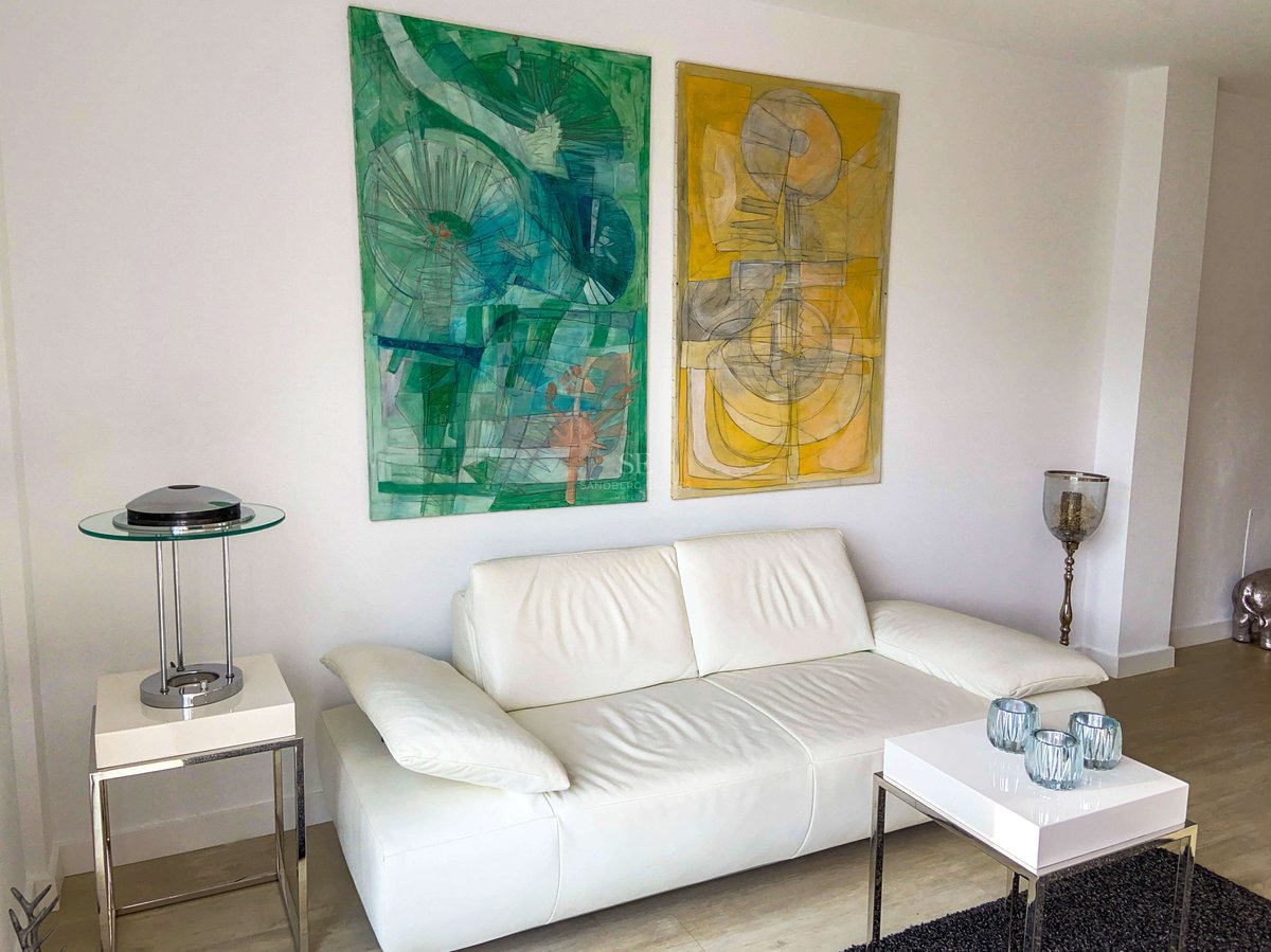 Weißes Ledersofa mit abstrakten Gemälden in Grün- und Gelbtönen sowie minimalistischen Chrommöbeln.