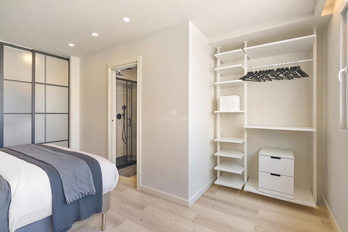 Helles modernes Schlafzimmer mit offenem weißem Schranksystem, hellem Echtholzparkett und Blick ins angrenzende Badezimmer.