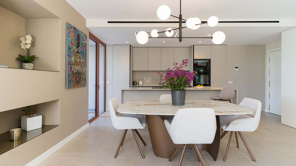 Contemporary dining room featuring a marble table, white chairs, and an integrated minimalist kitchen with pop art decor.