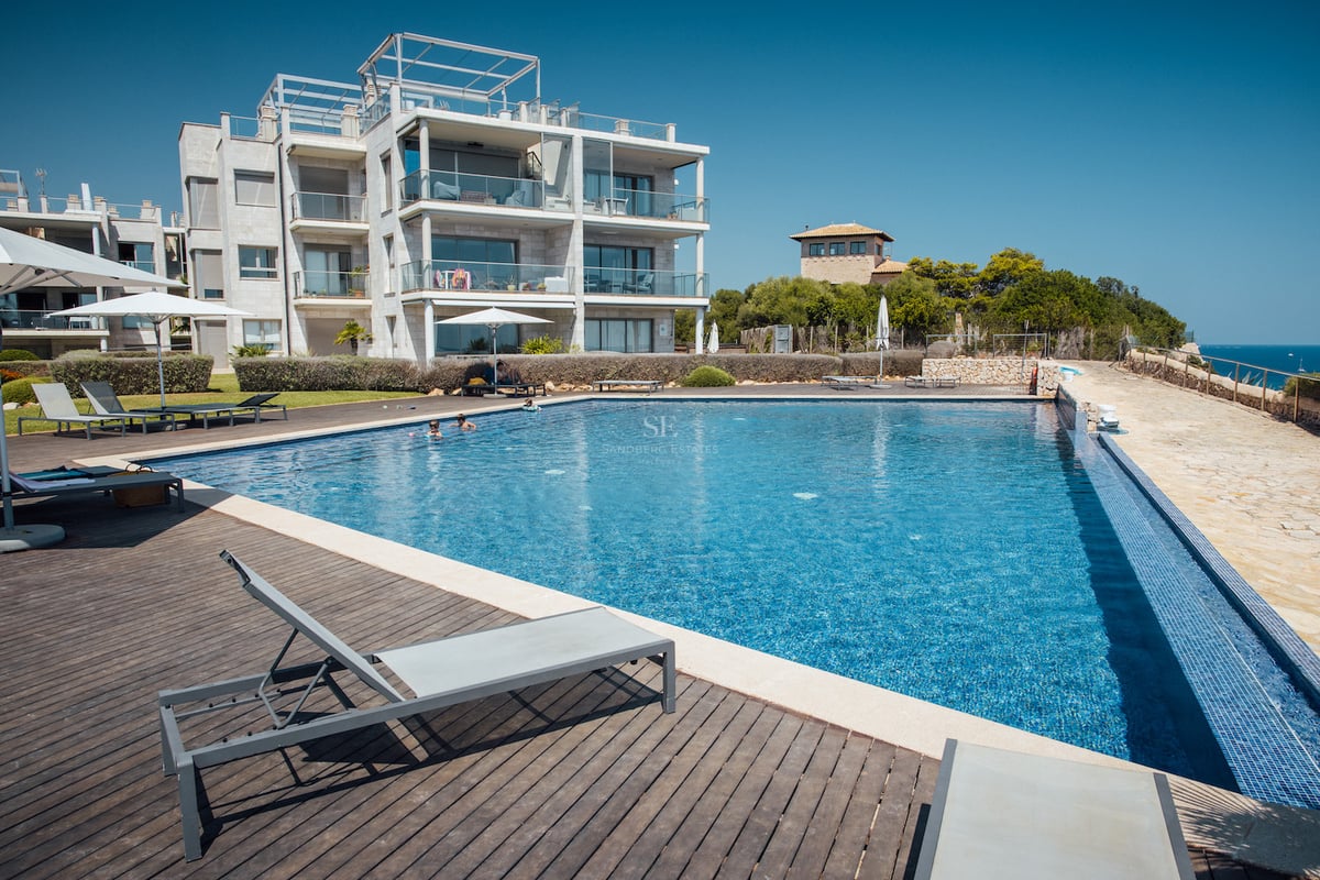 Grande piscine extérieure avec terrasse en bois, transats et immeuble d'appartements moderne par temps clair.